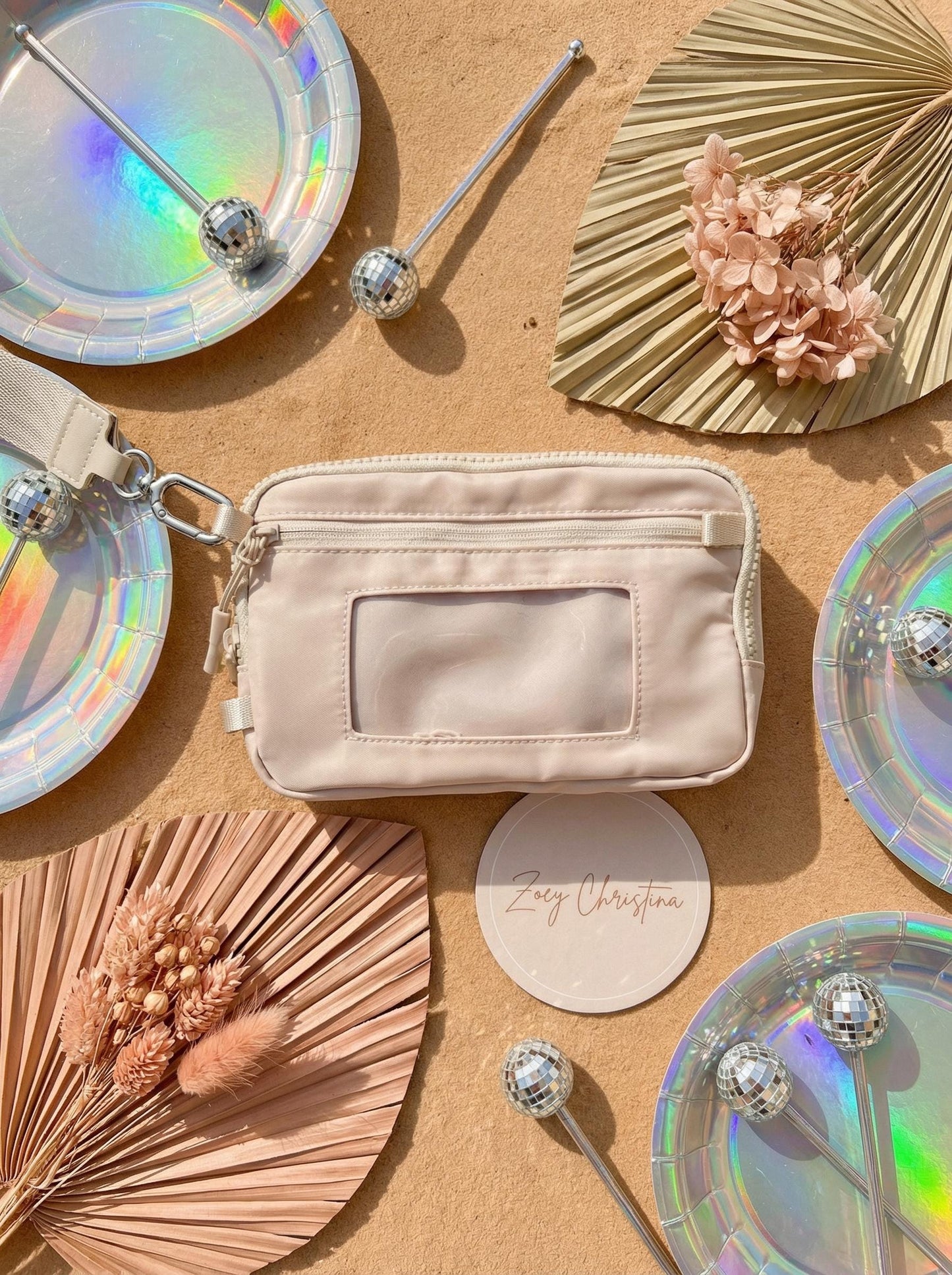 Beige pouch on a textured surface with decorative elements like iridescent plates and dried flowers.